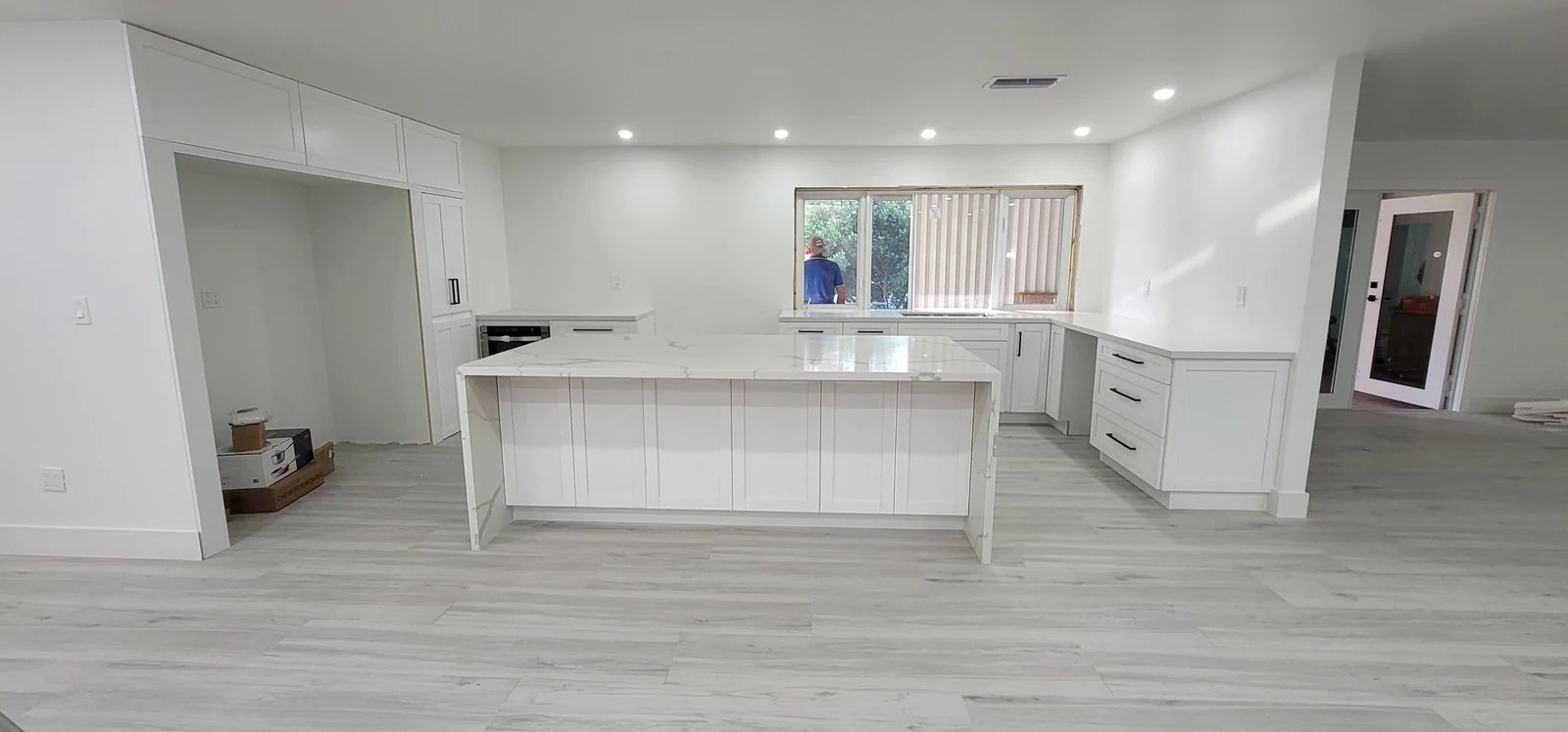 Wide view of a white kitchen with a long island and pale flooring