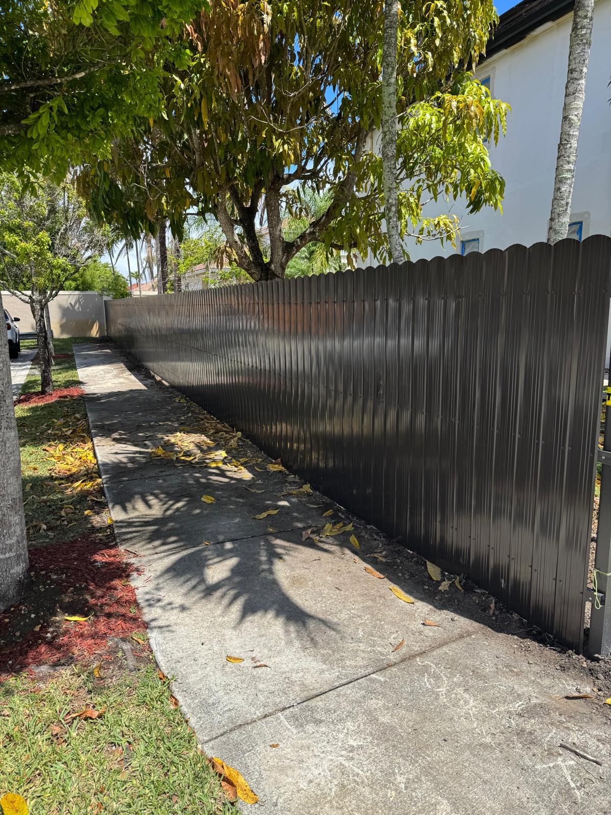 Long fence beside a shaded sidewalk